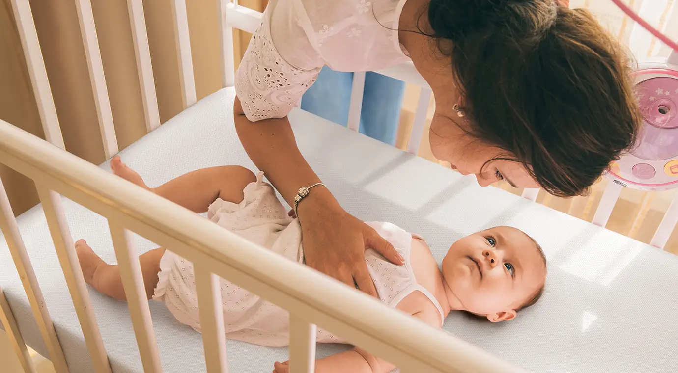 baby lying on numu air firm mattress for newborn looking at mother leaning over