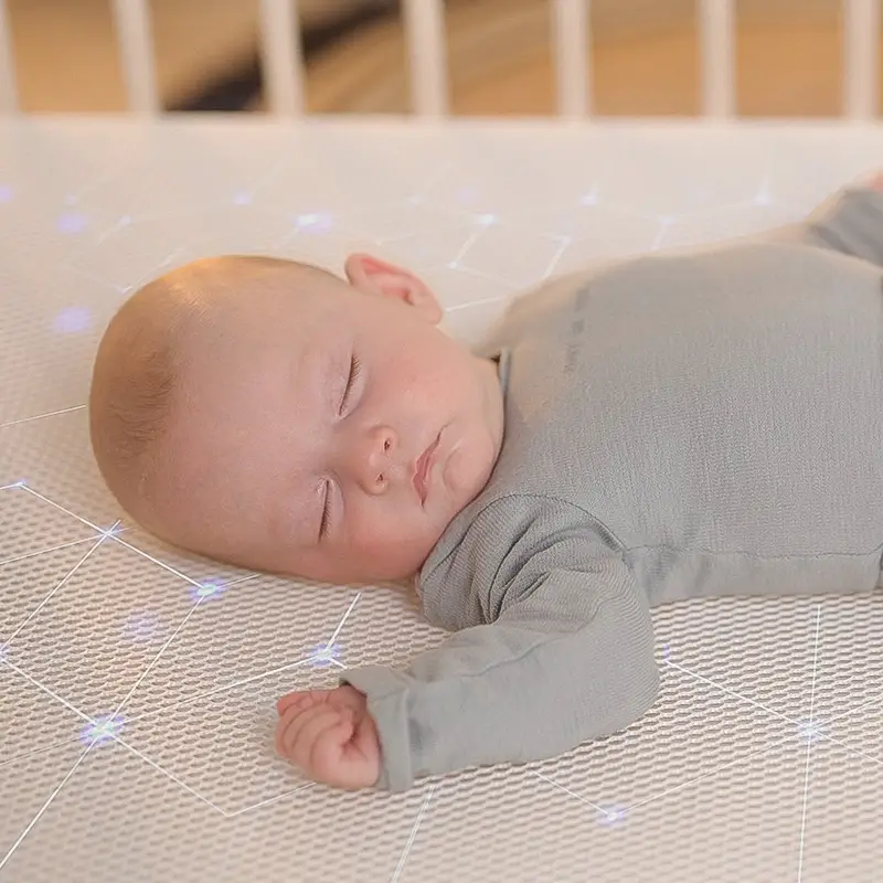 supine baby sleeping on numu air infant crib mattress that has glowing filaments