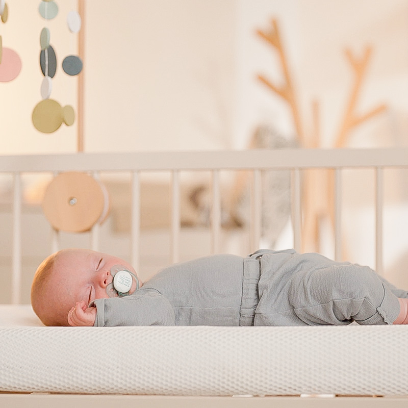 baby with pacifier sleeping on numu air non toxic crib mattress in supine position viewed from side