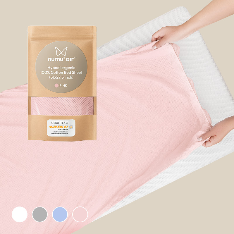 hands putting pink perforated breathe-through bedsheet on numu air infant crib mattress